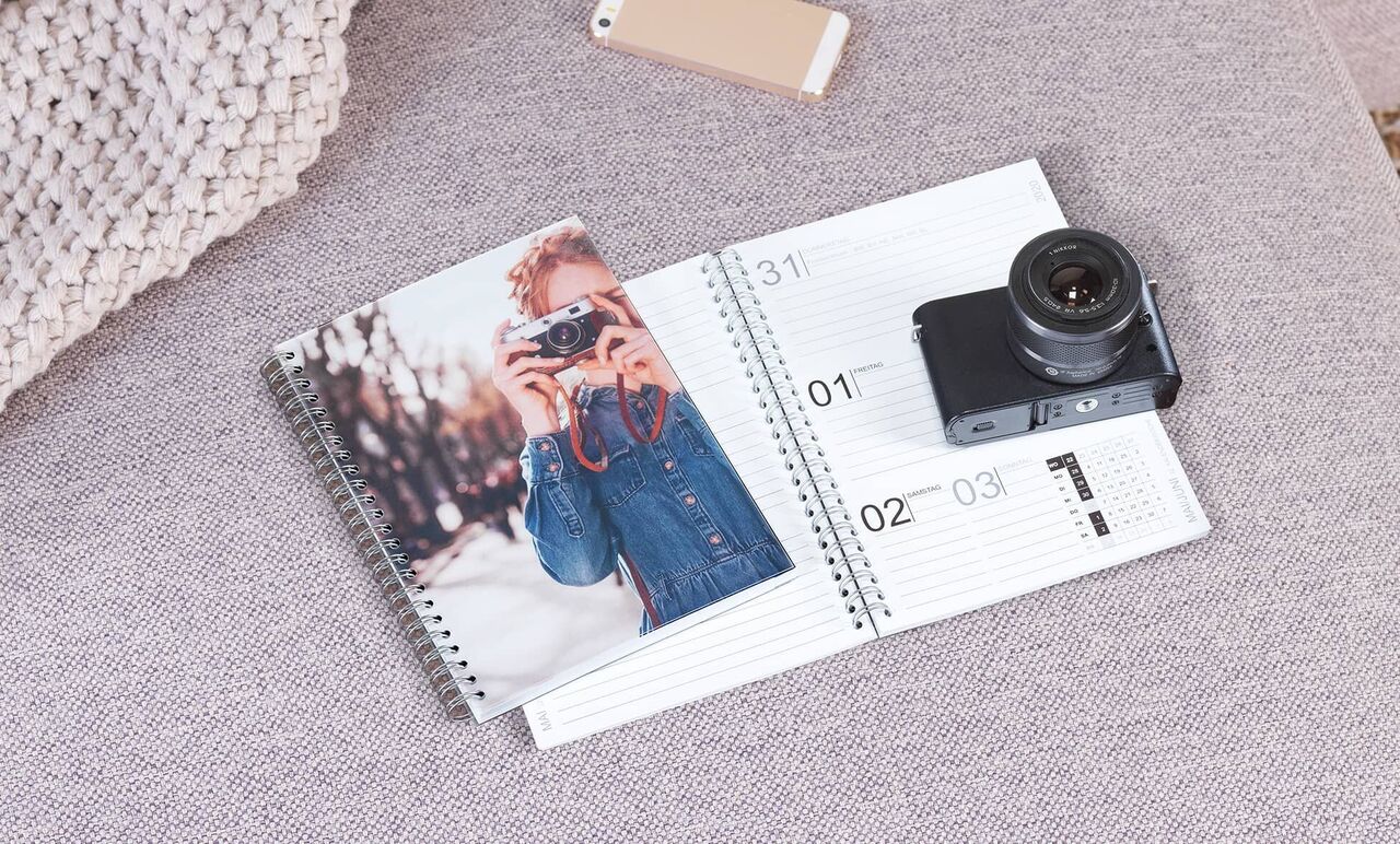 En fotokalender ligger på en grå soffa och visar ett foto av en leende fotograf.