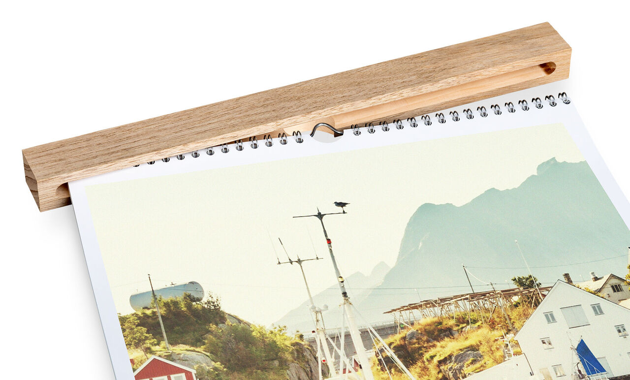 En CEWE fotokalender visar en pittoresk kustlandsbild med berg i bakgrunden.
