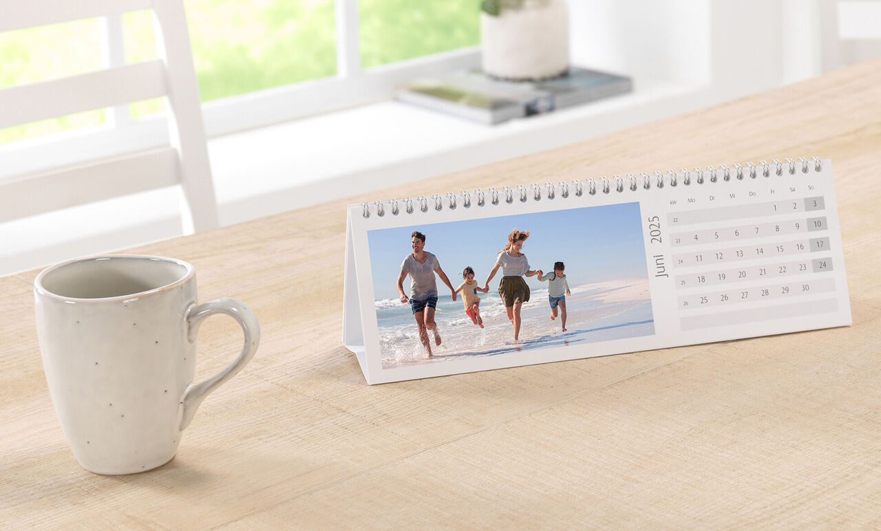 Familj går på stranden och njuter av sommaren. En CEWE fotokalender visar juni.