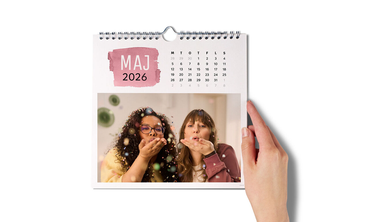 En hand som håller en väggkalender med ett glatt foto för maj 2025