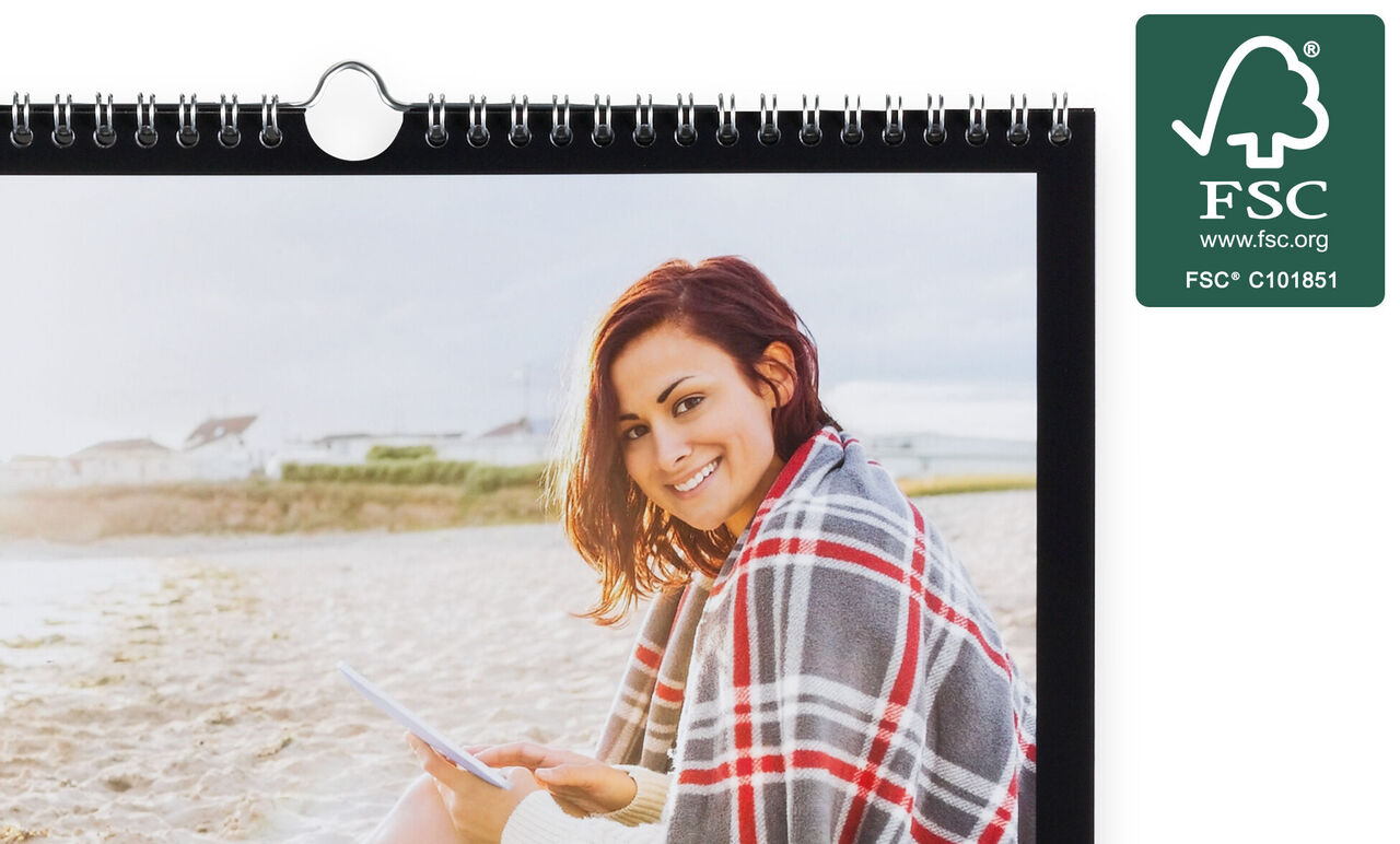 En person njuter av att koppla av på stranden med sin CEWE fotokalender bakom ryggen.