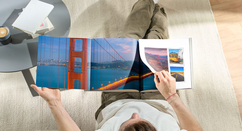 En person bläddrar i en CEWE fotobok med bilder av Golden Gate-bron och andra reseupplevelser.
