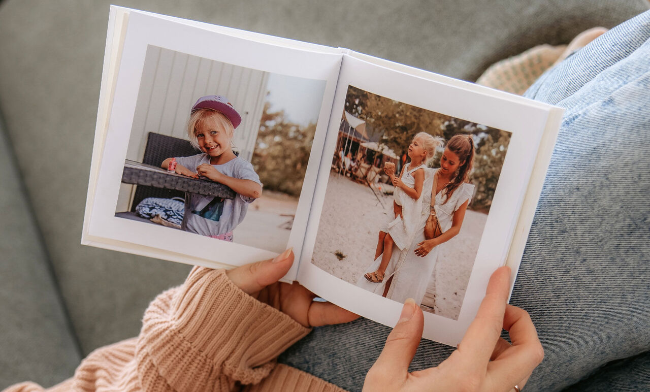 En person håller en öppen fotobok med två bilder. Den första bilden visar ett barn vid bordet och den andra en kvinna med ett barn.