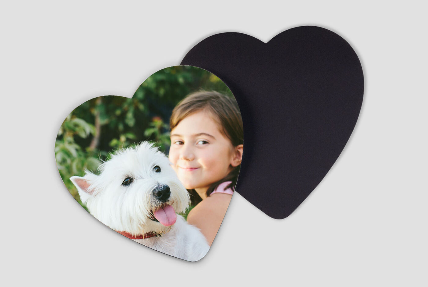En hund med vit päls och rosa tunga poserar framför en flicka på en hjärtformad kort