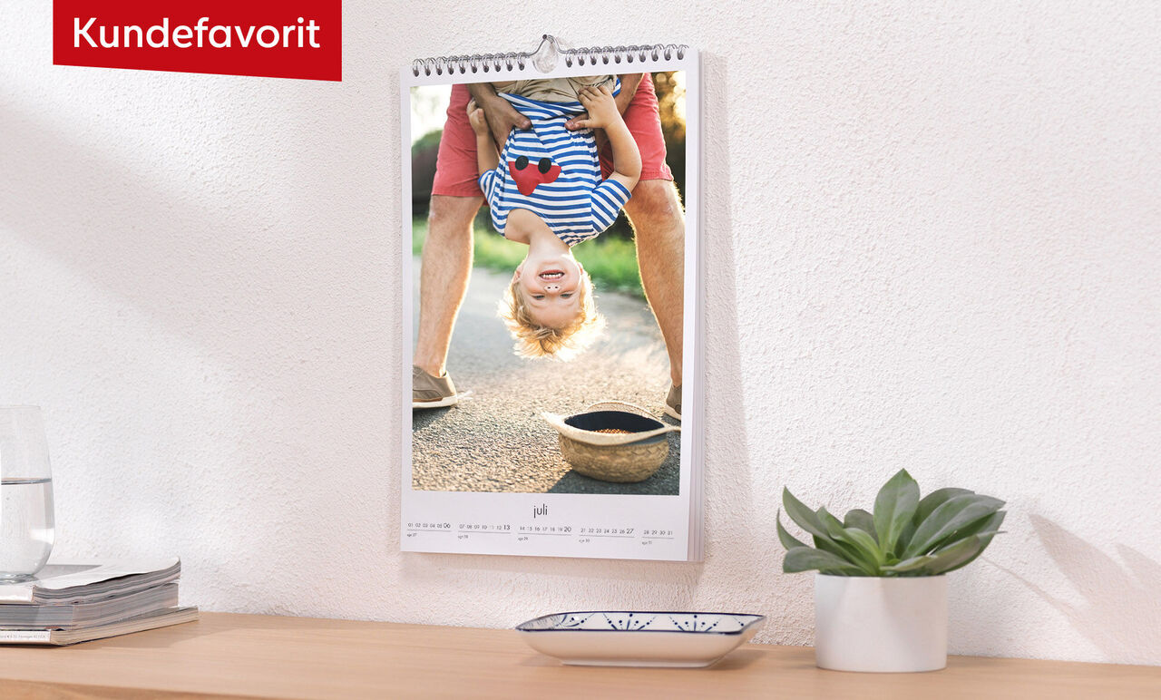 En upphängd väggkalender visar ett glatt barn som står på huvudet, med ett leende och ljusa strumpor.