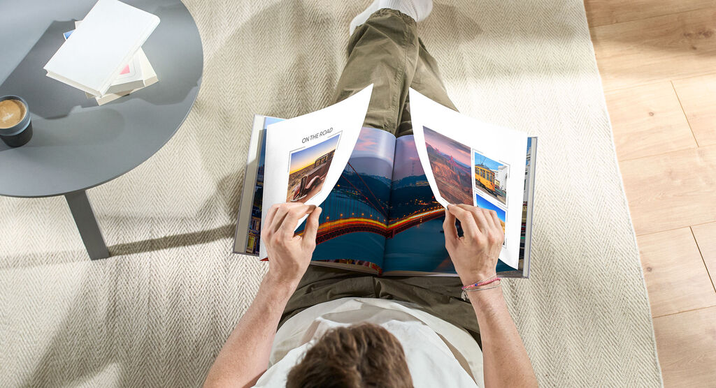 En person bläddrar i en öppen fotobok på golvet, omgiven av ett bord med en kopp.