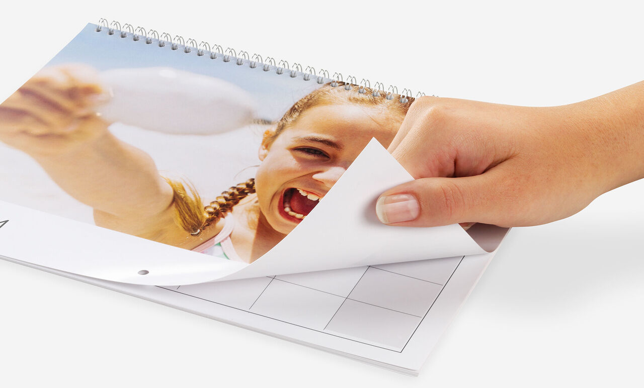En hand bläddrar igenom en fotokalender, glada semesterbilder synliga.