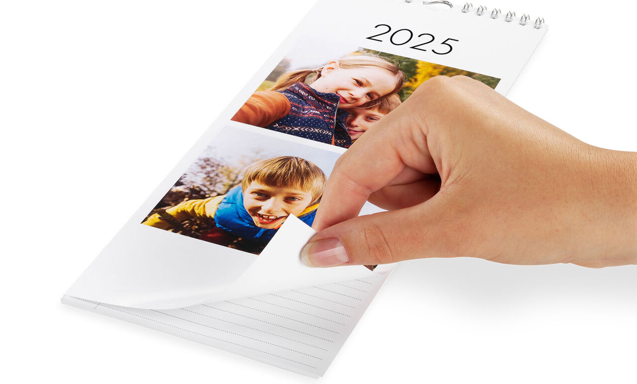En hand bläddrar genom en CEWE fotokalender för 2025 med bilder av lyckliga stunder.