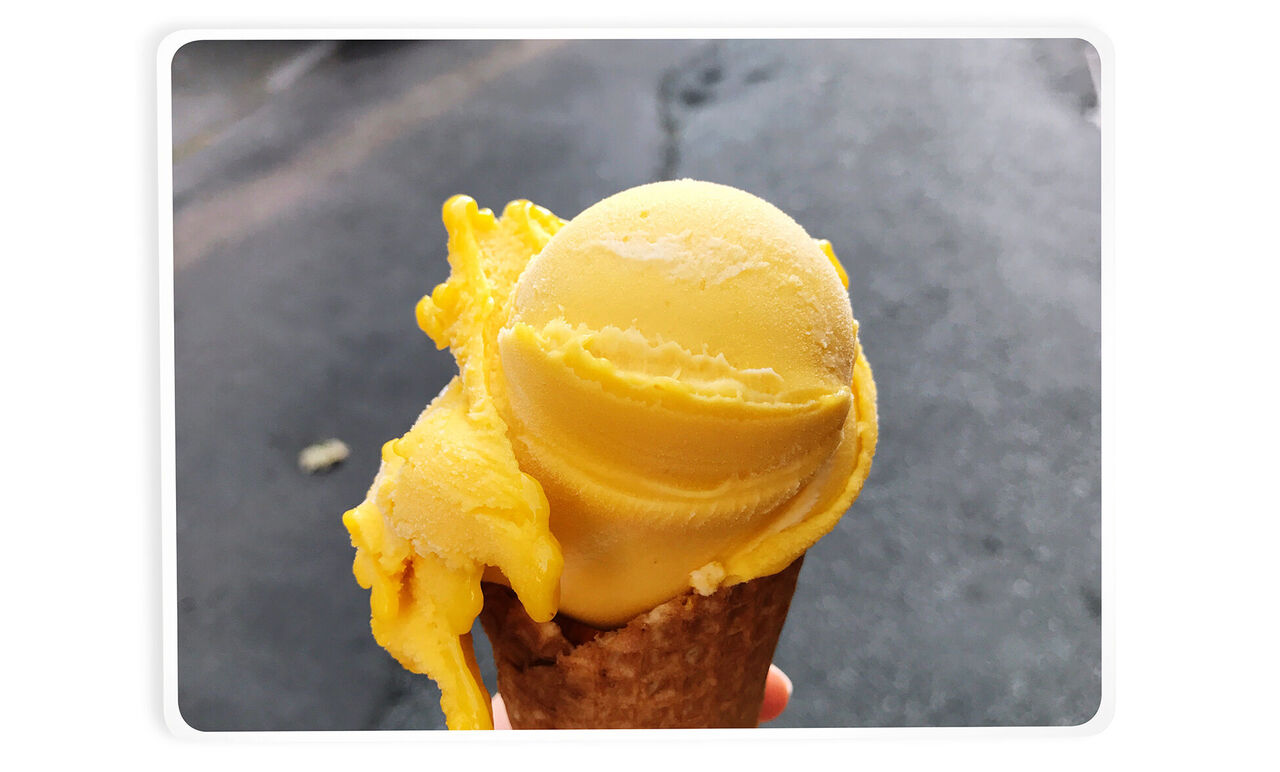 Glasskula av gul sorbet på en våffla i handen.