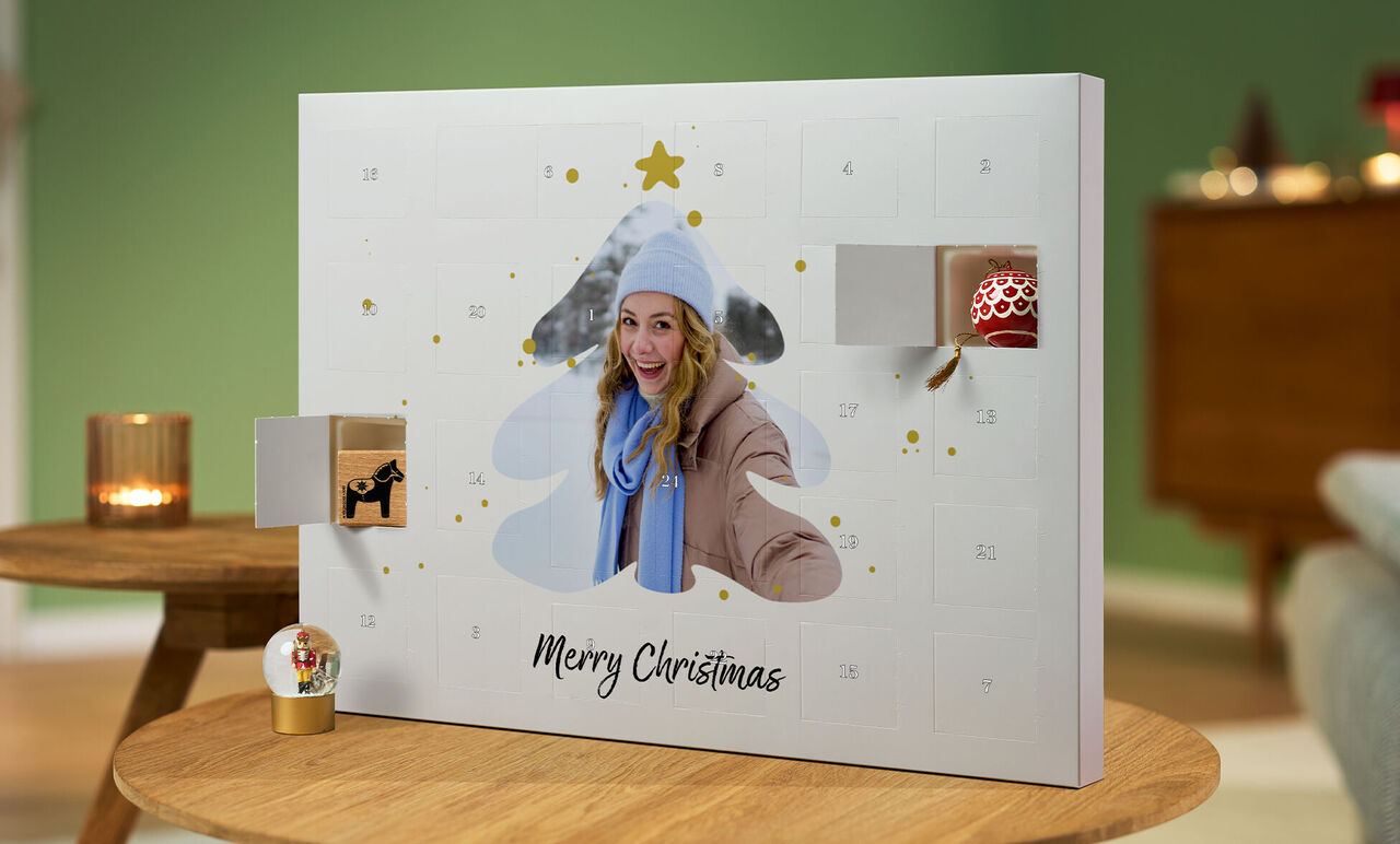 En öppen adventskalender i form av en julgran med paket och texten 'God Jul' i ett mysigt rum