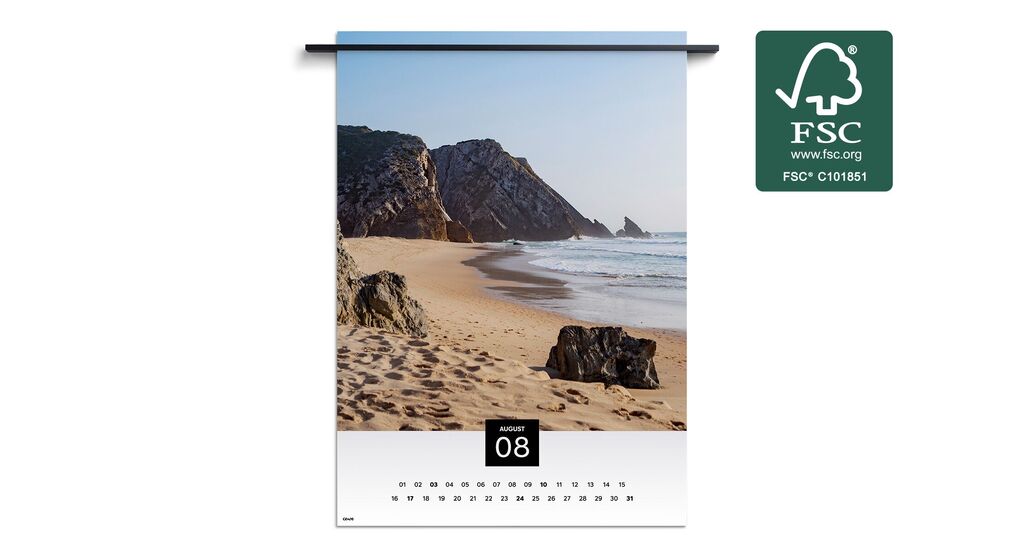 Strandlandskap med klippor och mjuka vågor under en blå himmel, avbildad i augusti månads väggkalender