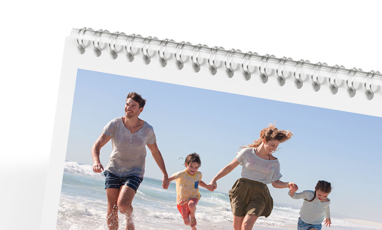 Familj går glatt längs stranden och njuter av solen. CEWE fotokalender.