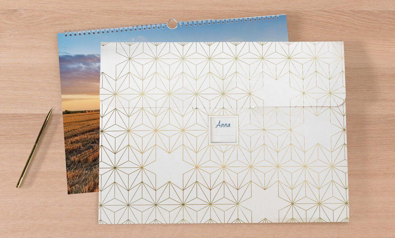 En stängd CEWE fotokalender på en träyta, bredvid ett foto och en guldspark.