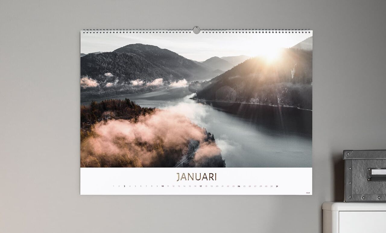 Ett kalenderblad för januari visar en vacker landskap med berg, dimma och soluppgång över vattnet.