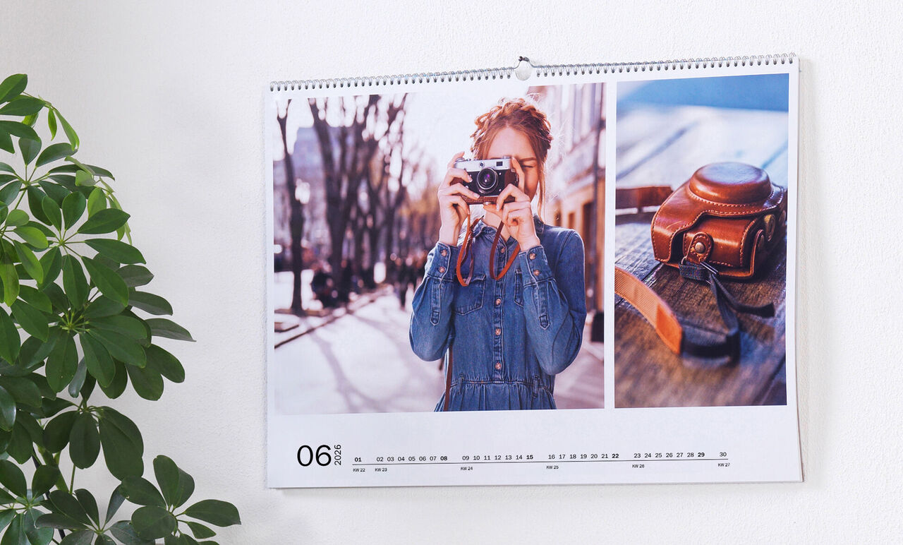 En väggkalender med en bild av en person som fotograferar och en gammal kamera på ett bord.