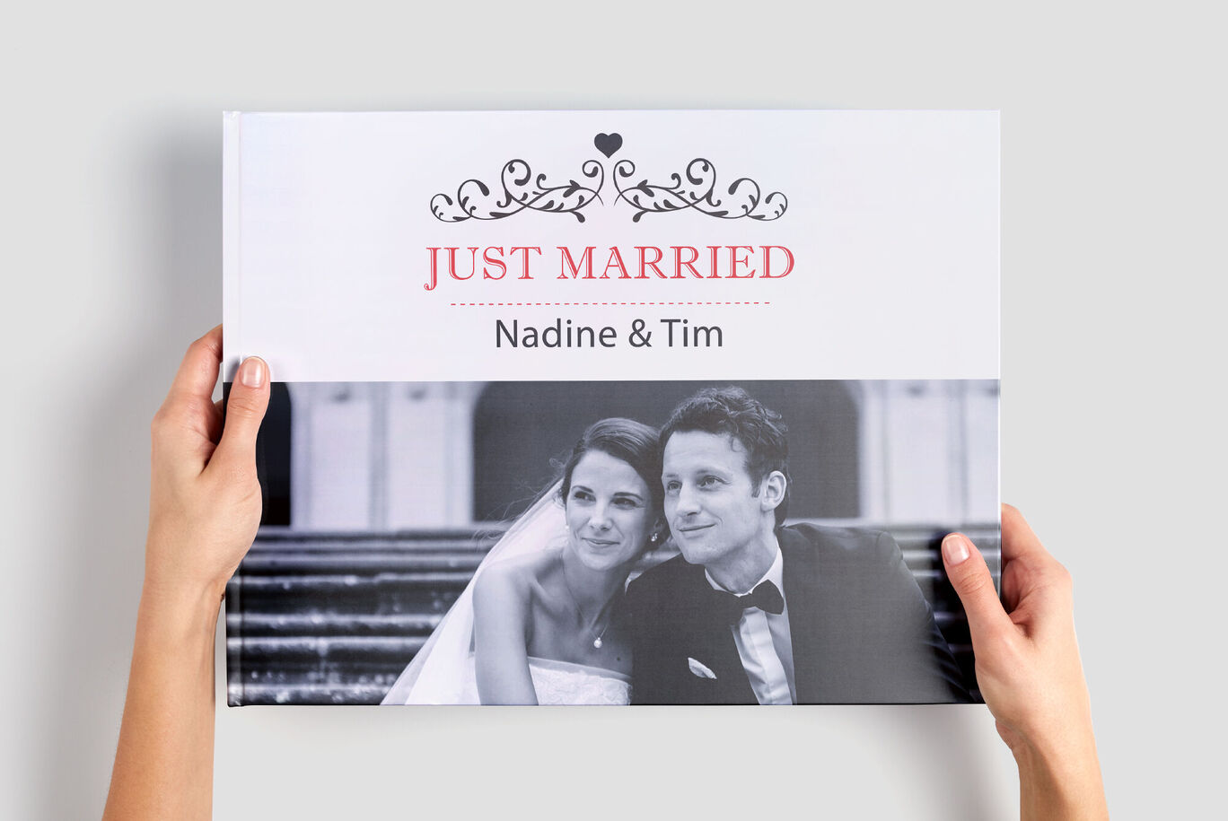 Händer håller en CEWE FOTOBOK med titeln 'Just Married' och namnen 'Nadine & Tim'