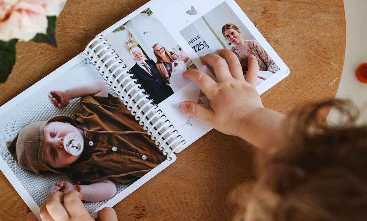 Ett barn visar en sida av en fotobok med familjebilder och minnen.