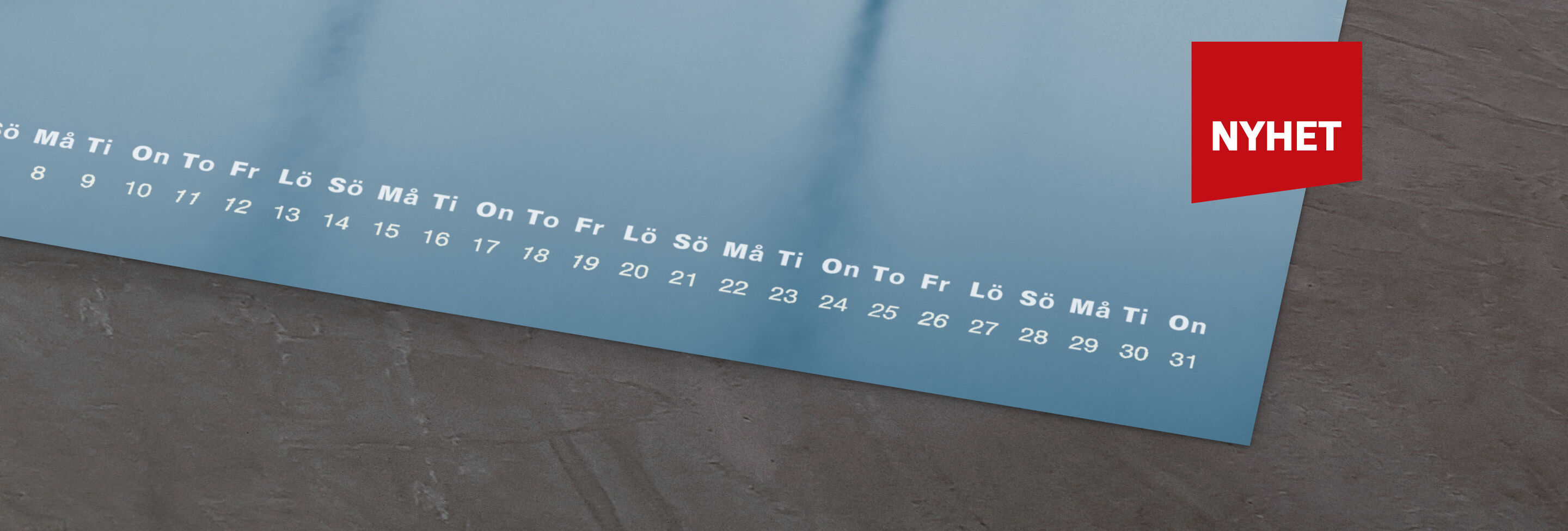 Kalender med blå bakgrund och veckodagar, röd "NY" klistermärke i hörnet.
