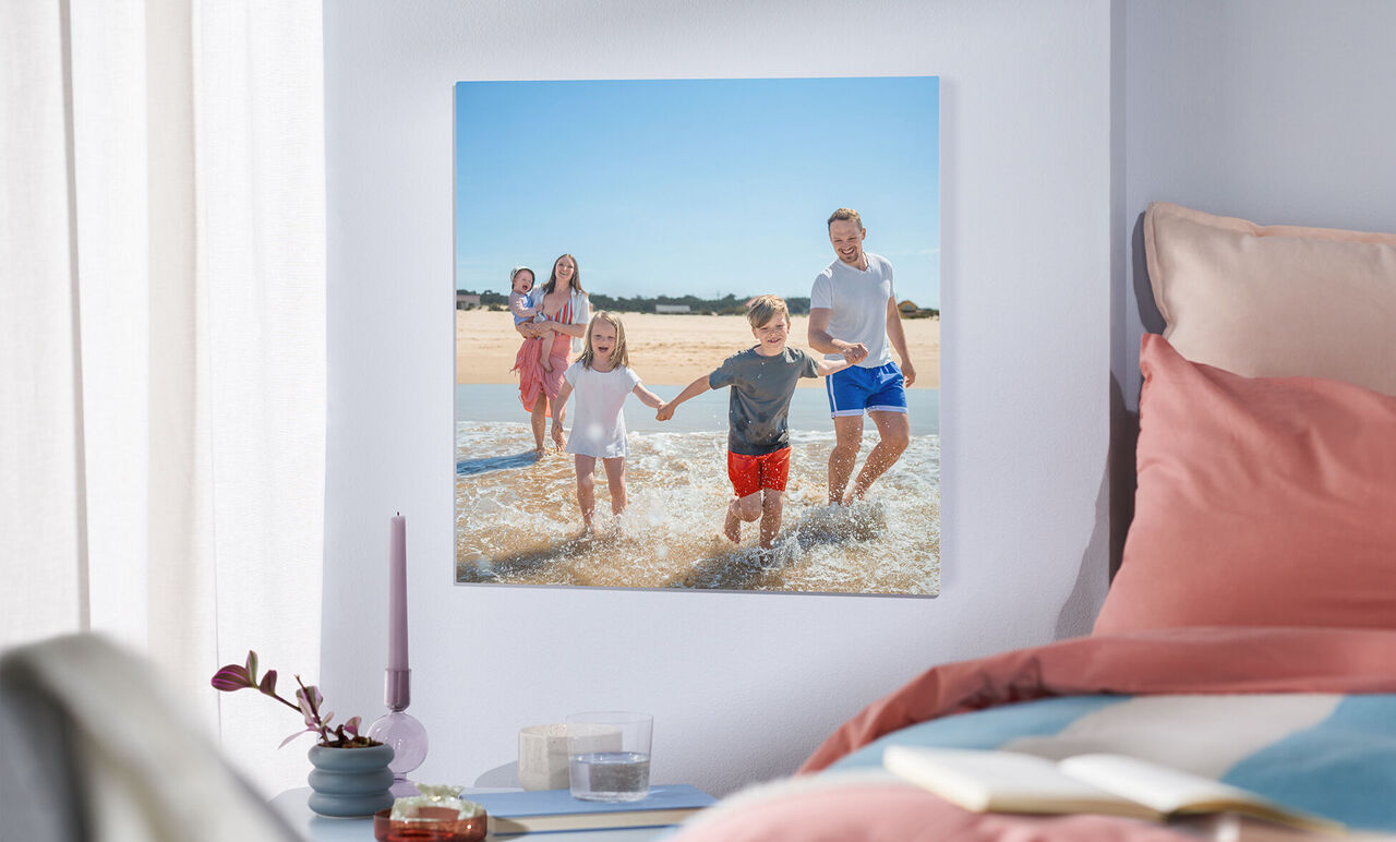 En lycklig familj leker i vattnet på stranden. Två vuxna och två barn håller händer. Solen skiner.