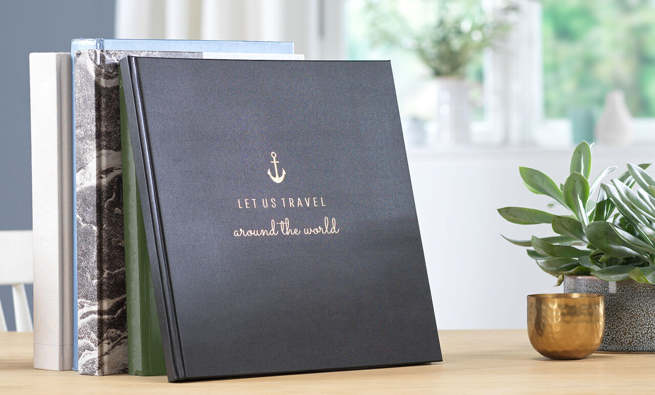 Svart fotoalbum med titeln 'Låt oss resa jorden runt' på ett bord