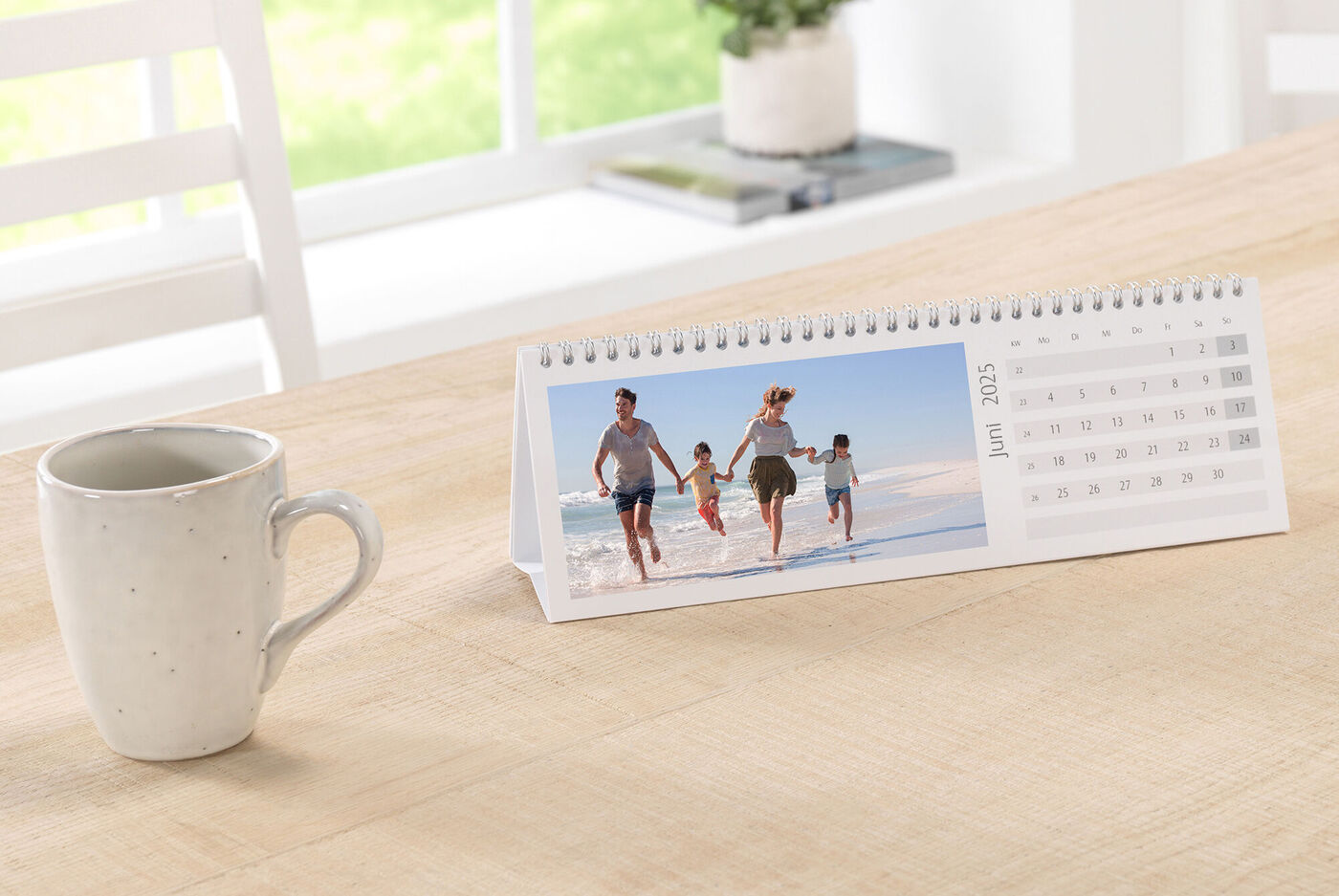 En CEWE fotokalender på ett bord visar en glad familj som går längs stranden.