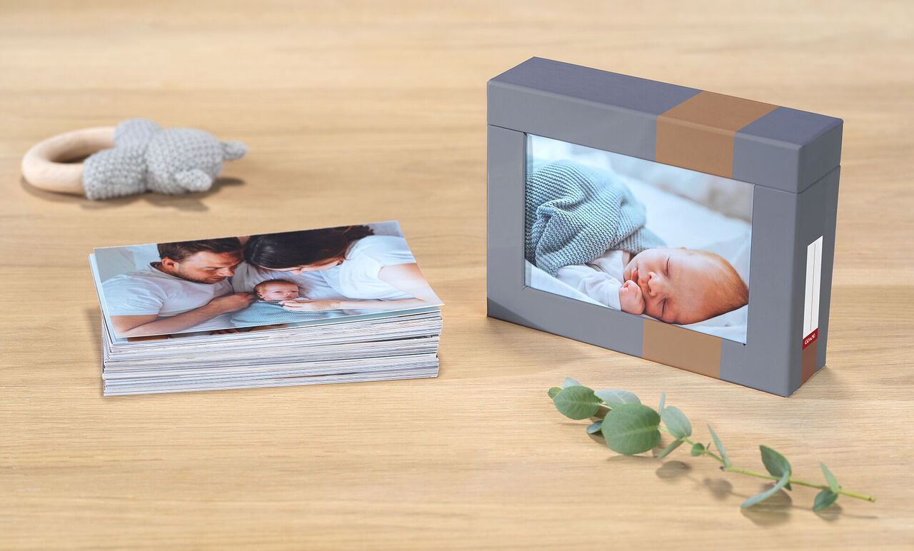 CEWE fotobok med bilder av en nyfödd och familj på ett träbord, intill en låda med en bild av den sovande babyn.